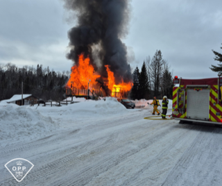 House engulfed in flames, thick black smoke rising, firefighters on scene, snowy landscape