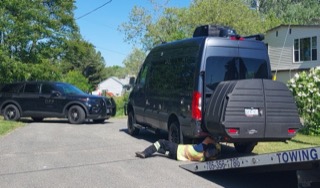 Black van with a person working underneath. Police car visible in the background.