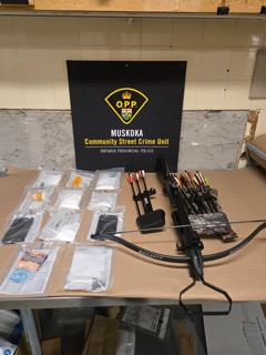 Muskoka Community Street Crime Unit, Ontario Provincial Police. Bow and arrows, assorted drugs in baggies, cash, and a knife on a table.