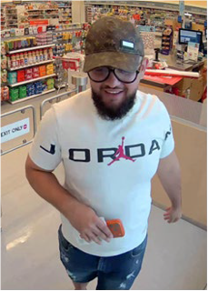 Man wearing a white t-shirt with &quot;Jordan&quot; printed on it, distressed jeans, and a baseball cap; smiling and holding a small orange object.