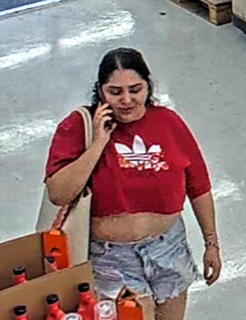 Woman on phone, wearing a red t-shirt with a white Adidas logo and denim shorts.