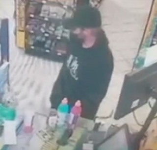 Person in a black hoodie and hat, standing near bottled drinks