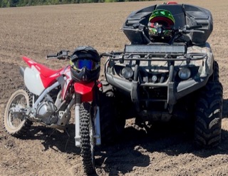 Dirt bike and ATV parked on dirt.