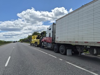 Semi-truck and trailer stopped on highway, tow truck behind