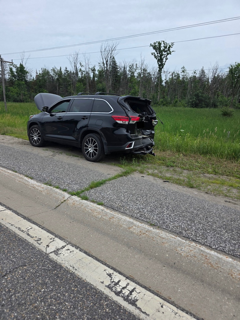 Black SUV with damaged hood and rear bumper on the side of a road.