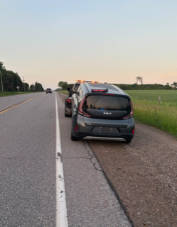 Black minivan with emergency lights on, parked on the shoulder of a rural road