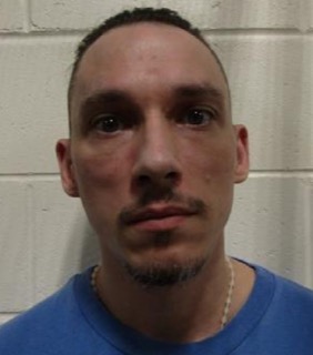 Man with a short haircut and goatee, wearing a blue t-shirt and a silver chain.