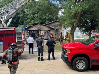 Firefighters and police officers assess a house with smoke damage.