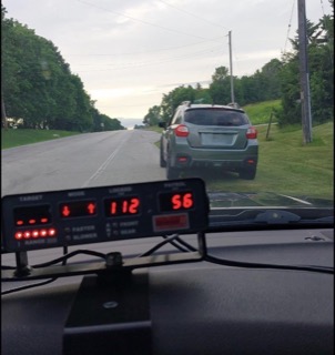 Gray SUV driving on a two-lane road, green trees lining the sides