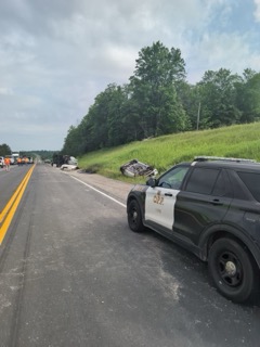 Damaged vehicle off the shoulder of a highway, police vehicle present